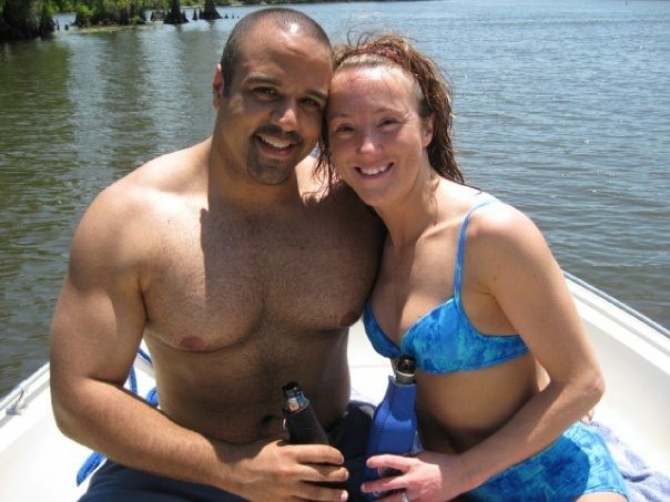 Ray and Rebecca sitting close together on a boat, smiling, with trees along the water behind them.